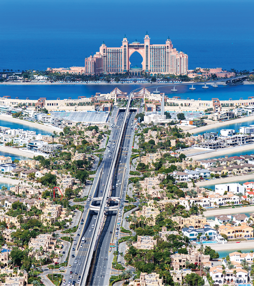 Aerial view of a multi-lane highway leading to Atlantis, The Palm hotel on a man-made island in Dubai, with blue sea in the background and surrounding residential areas.